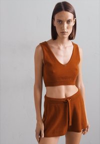 Pletena crop majica rust boje s V-izrezom i pripadajućim šortsevima sa vezicom, koji imaju mekanu teksturu i minimalistički dizajn.