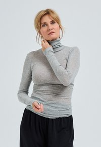 Maglione grigio chiaro a maniche lunghe con colletto a dolcevita realizzato in materiale morbido e elasticizzato. Presenta un design aderente con una texture liscia e una vita arricciata.