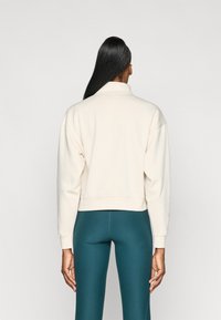 Sweatshirt crème, court, avec un col montant et des épaules tombantes. Assorti à des leggings vert foncé. Texture de tissu lisse et doux.