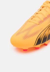 Fodboldstøvle i lys orange med sorte og pink accentstriber. Har en struktureret syntetisk overdel og kontrasterende pink studs.