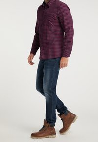 Czerwona i granatowa koszula w kratę z długimi rękawami, połączona z ciemnoniebieskimi dżinsami i brązowymi butami sznurowanymi z teksturowaną podeszwą.