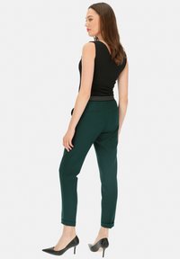 Czarny top bez rękawów, zielone dopasowane spodnie z podwiniętymi nogawkami i czarne szpilki, widok z tyłu.