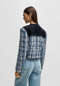 Blå og hvid ternet cropped jakke med tekstureret stof, sort strikket yoke, lange ærmer og rå kantdetaljer. Bæres med højtaljede jeans.