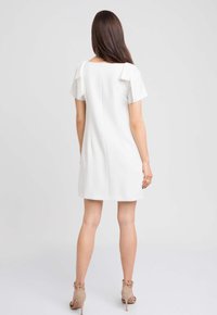 Biała sukienka z krótkim rękawem z zaokrąglonym dekoltem, zamek błyskawiczny z tyłu oraz kokardą na rękawach. Gładki, strukturalny materiał.