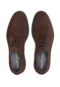 Zapatos de ante marrón con una textura suave, punta redonda y cordones negros. Presentan un sutil detalle de marca en el interior. Diseño clásico, suela sólida.