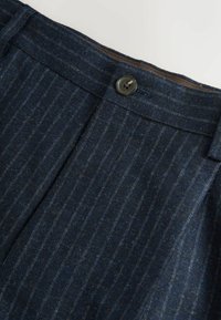 Tumši zilas pielāgotas bikses ar svītru rakstu, kas aprīkotas ar pogu aizdari un gludu auduma tekstūru.