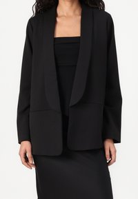 Černý blazer s otevřeným předním designem, dlouhými rukávy a dvěma předními kapsami. Vyrobeno z hladké, strukturované tkaniny s minimalistickou estetikou.