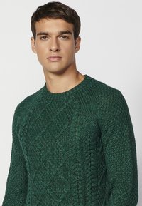 Groene gebreide trui met een gestructureerd ruitpatroon; heeft een geribbelde ronde hals en lange mouwen, gemaakt van een dik, comfortabel materiaal.