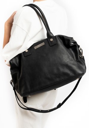 Sac à main en cuir noir avec deux bretelles, accessoires en métal argenté et un accent clouté sur le devant. Il comprend une bandoulière amovible.