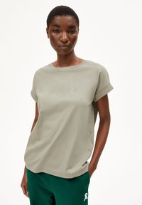 T-shirt en coton kaki avec des manches courtes retroussées et un col rond ; présente un discret logo brodé sur la poitrine ; texture lisse.