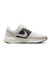 Zapatilla de running ligera en beige y verde oscuro. Parte superior de malla texturizada, suela acolchada, puntera reforzada y un logo prominente en el lateral.