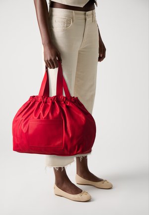 Bolsa de couro vermelha com um topo franzido e um bolso frontal, apresentando alças vermelhas duplas. Textura suave com um acabamento brilhante.