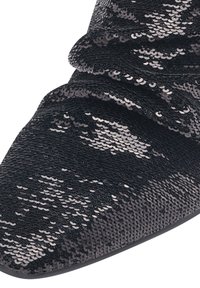 Zapato negro con lentejuelas, que presenta una punta afilada y una textura recogida. La parte superior está cubierta de lentejuelas brillantes y superpuestas, que reflejan la luz.