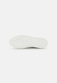 Suola di sneaker bianca con design in gomma testurizzata, caratterizzata da motivi in rilievo e branding. Superficie liscia con un grip confortevole.