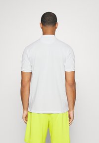 Hvit kortermet polo-skjorte med krage og subtil tekstur; kombinert med lysegule treningsshorts. Rent og minimalistisk design.