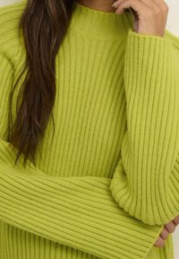 Sweter z prążkowanej dzianiny w kolorze limonkowym, z wysokim dekoltem i długimi rękawami, cechujący się fakturowanym materiałem i lekko oversize'owym krojem.