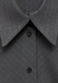 Tissu gris foncé à rayures fines, avec un col pointu et deux boutons noirs sur un vêtement ajusté.