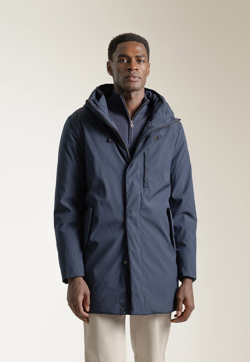 Parka impermeable azul marino con capucha, cierre delantero y bolsillos laterales. Presenta una tela texturizada y un ajuste ligeramente holgado.