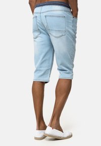Pantalones cortos de mezclilla azul claro con una cintura oscura, de longitud hasta la rodilla, diseño de cinco bolsillos y una textura ligeramente descolorida en el tejido.