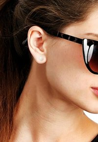 Lunettes de soleil noires et écaille de tortue, monture surdimensionnée, verres foncés dégradés. Boucle d'oreille en perle simple, texture de peau lisse, vue de profil.