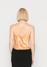 Camisola de cetim laranja com um design cruzado nas costas, apresentando um padrão em espiral, textura suave e uma silhueta fluida. Combinada com uma saia preta.