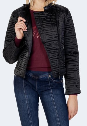 Frau trägt dunkelblaue Jeans, burgunderroten Pullover und teilweise geöffneten schwarzen Steppjacke.