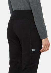 Zwarte sportbroek met een gladde textuur, voorzien van een brede tailleband, versterkte stiksels, zijzak en een klein logo-detail.