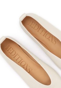 Ζευγάρι λευκές δερμάτινες μπαλαρίνες χωρίς κορδόνια με ταμπά ενισχύσεις εσωτερικά, με το λογότυπο "Kazar EDITIONS" ορατό στο εσωτερικό, φωτογραφημένες από πάνω σε λευκό φόντο.