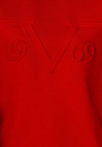 Red sweatshirt featuring raised text "V" and "1969." Soft texture, long sleeves, and a round neckline with a casual design.