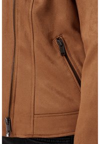 Bruine suedjas met een ritssluiting en een contrasterende zwarte rits, met een gladde textuur en een aansluitend ontwerp.