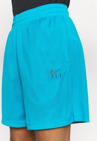 Blå mesh träningsshorts med elastiskt midjeband och liten svart Nike-logga samt texten "FLY" på vänster lår, bärs med en svart topp.