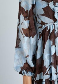 Vestido floral con un patrón azul y marrón, fabricado en un tejido ligero, con mangas con volantes y una cintura fruncida para mayor textura.
