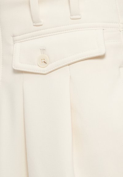 Τραβηγμένο μπροστά, με πιέτες και διακοσμητική τσέπη με κούμπωμα κουμπιού, παντελόνι σε κρεμ απόχρωση. Λείο, δομημένο ύφασμα.