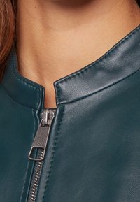 Teal leather jacket with a stand collar, featuring a silver zipper and stitching details, highlighting smooth texture and sleek design.