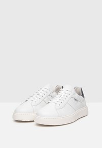 Sneaker bianchi in pelle con design a taglio basso, punta rotonda, chiusura con lacci e dettagli grigi sul tallone. Dettagli laterali testurizzati.