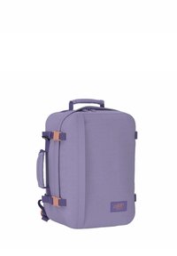 Zaino da viaggio viola realizzato in tessuto resistente, di forma rettangolare, dotato di maniglia superiore, cinturini laterali e accenti marroni.