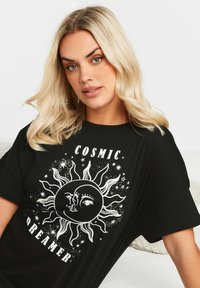 T-shirt nera con una grande grafica bianca di un sole, che presenta elementi facciali artistici, stelle e il testo "COSMIC DREAMER." Maniche corte.