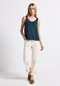 Turkusowy top bez rękawów z szerokimi ramiączkami, zestawiony z kremowymi spodniami z podwiniętymi nogawkami oraz brązowymi butami wsuwanymi. Gładki, lekki materiał.