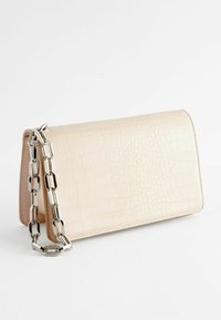 Pochette en simili cuir crème gaufré crocodile avec une chaîne en métal argenté, présentant une forme rectangulaire structurée et des coutures soignées.