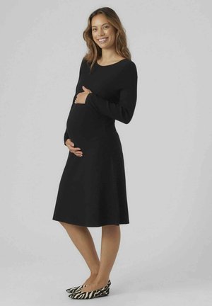 Schwarzes langärmliges Kleid mit tailliertem Oberteil, ausgestellt Rock und glatter Textur. Kombiniert mit flachen Schuhen im schwarz-weißen Zebra-Druck.