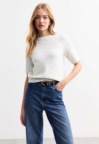 Ljust grå kortärmad stickad tröja med rund halsringning, matchad med blå högmidjade jeans i denim, accentuerad av ett svart bälte med guldfärgade detaljer.