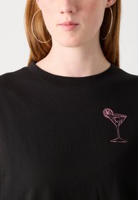 Black cotton t-shirt featuring a pink embroidered graphic of a cocktail glass with a lime slice and the word "Boss" below it.