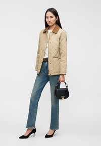 Μπεζ καπιτονέ μπουφάν με καφέ γιακά, λευκό πουκάμισο, μπλε τζιν και μαύρα τακούνια. Το μοντέλο κρατά μια μικρή μαύρη τσάντα με χρυσά μεταλλικά στοιχεία.