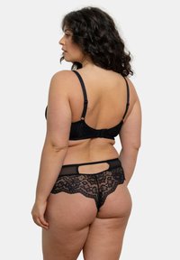Soutien-gorge en dentelle noire et culotte transparente assortie, mettant en avant un délicat motif floral, des bretelles lisses et une découpe en forme de clé au dos.