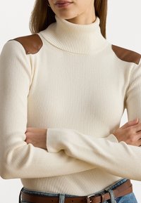 Ribbed cream turtleneck-neule, jossa on ruskeat nahkaolkapäät; istuvat hihat ja vartalo, pehmeällä tekstuurilla.