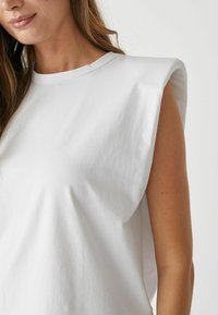 White cotton sleeveless top with a round neckline, featuring structured shoulder details and a smooth, slightly loose fit.
