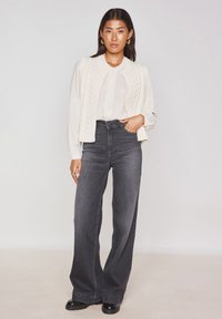 Gilet en tricot crème sur un blouse légère, associé à un jean large taille haute gris foncé et des chaussures à plateforme noires.