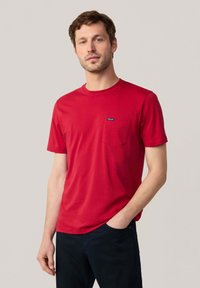 Rotes Baumwoll-T-Shirt mit Rundhalsausschnitt, kurzen Ärmeln und einer Brusttasche auf der linken Seite. Verfügt über ein kleines blaues Logo-Etikett auf der Tasche.