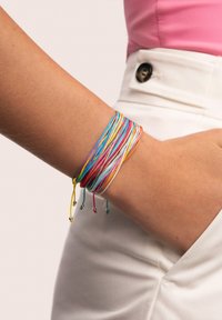 Braccialetti di corda colorata in varie tonalità, caratterizzati da più filamenti e accenti in argento, avvolti attorno a un polso su uno sfondo chiaro.
