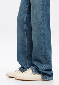 Light-wash denim jeans with a straight-leg cut and distressed hem, paired with white sneakers featuring a textured sole and laces.